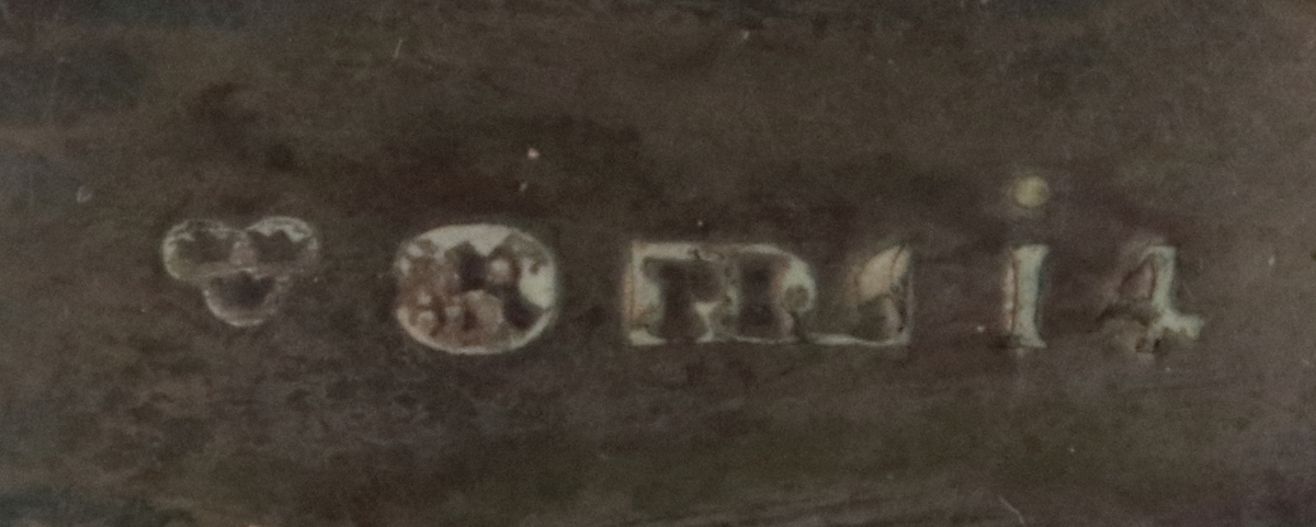 Oval ask i silver. Namnen "P Andersson" och "AC Andersdoter" är inristade på lockets ovansida, omgivna av en dekorativ bård med triagulära mönster. Asken är stämplad på botten på insdian av asken med kattfot, i4 (år 1839) och två svårtydda stämplar.