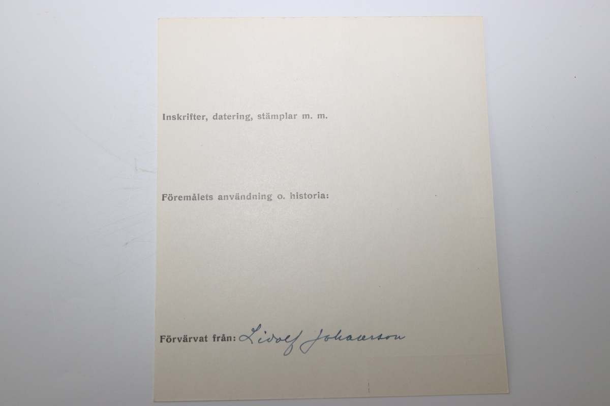 Oval ask i silver. Namnen "P Andersson" och "AC Andersdoter" är inristade på lockets ovansida, omgivna av en dekorativ bård med triagulära mönster. Asken är stämplad på botten på insdian av asken med kattfot, i4 (år 1839) och två svårtydda stämplar.