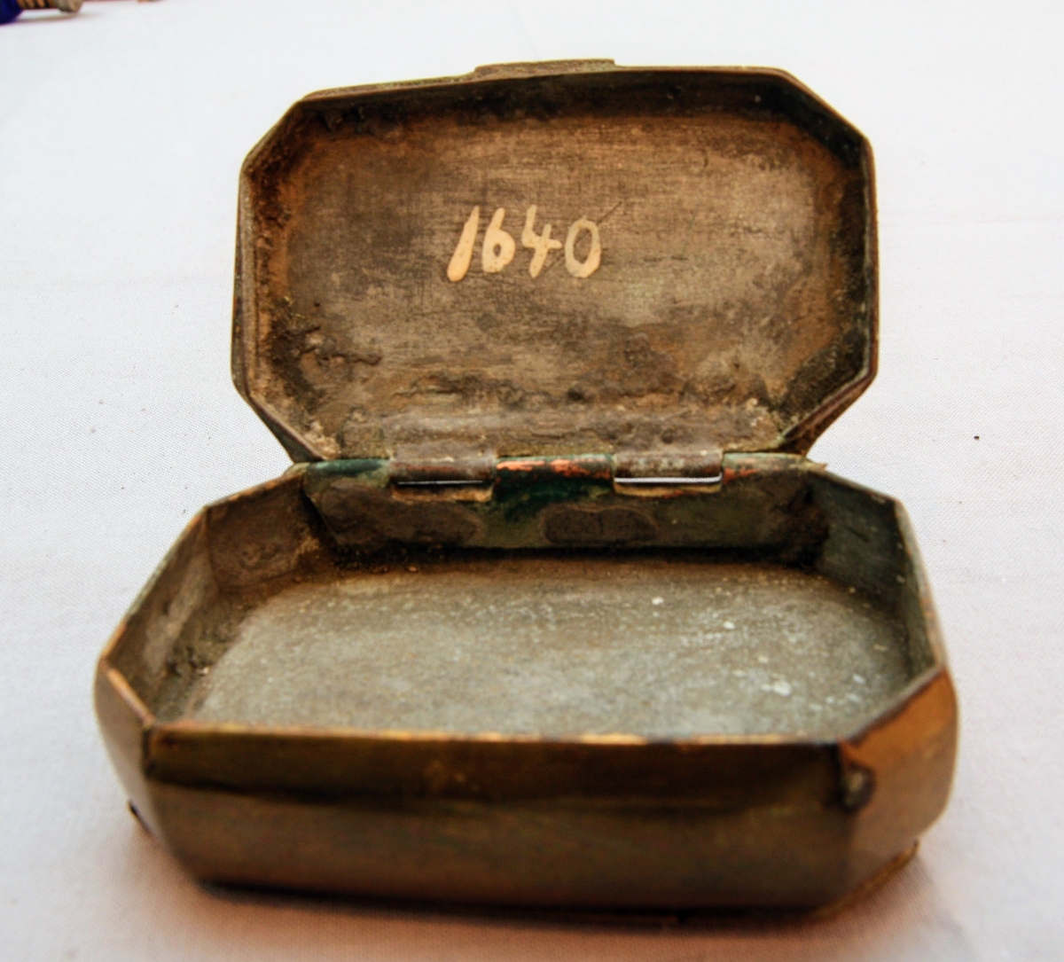 Tobaksdosa i mässing med uppfällbar spegel. Asken öppnas med ett lock i botten. Med gångjärn i ena hörnet där stödet till den uppfällbara spegeln är gängat.  Inskription i botten med bokstäverna ”APL" och siffrorna 1873 efter. Förutom inskriptionen finns inga dekorativa element på föremålet.