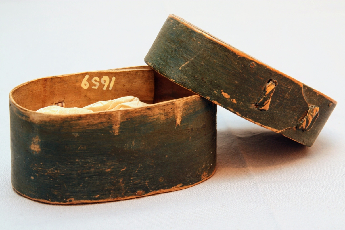 En oval ask av svept spån. Grönmålad, locket har röd kant, i mitten är en enkel ros målad. Äskan innehåller en fingerring, två mindre spännen, öronringar och ett litet hängsmycke i form av ett hjärta.