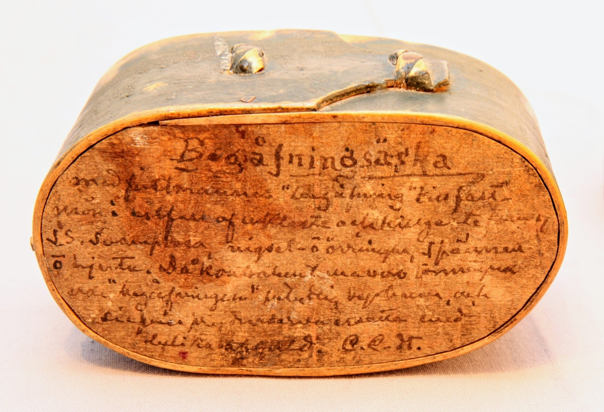 En oval ask av svept spån. Grönmålad, locket har röd kant, i mitten är en enkel ros målad. Äskan innehåller en fingerring, två mindre spännen, öronringar och ett litet hängsmycke i form av ett hjärta.