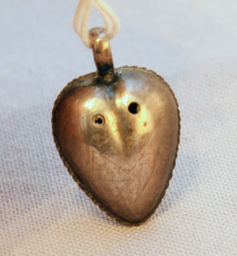 En oval ask av svept spån. Grönmålad, locket har röd kant, i mitten är en enkel ros målad. Äskan innehåller en fingerring, två mindre spännen, öronringar och ett litet hängsmycke i form av ett hjärta.