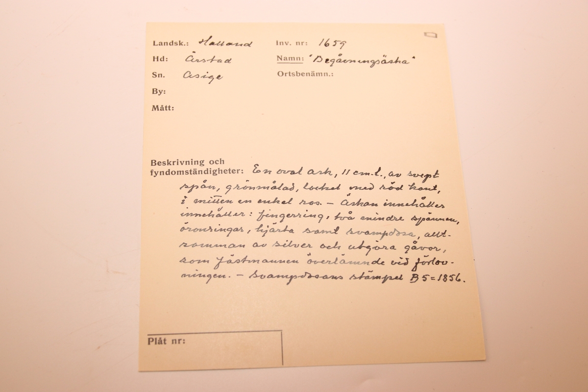 En oval ask av svept spån. Grönmålad, locket har röd kant, i mitten är en enkel ros målad. Äskan innehåller en fingerring, två mindre spännen, öronringar och ett litet hängsmycke i form av ett hjärta.