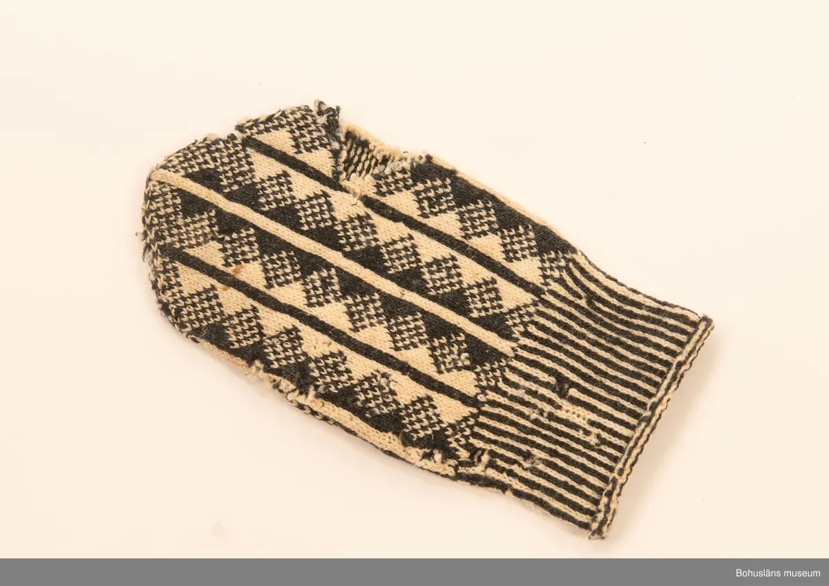 Handstickad mönstad tumvante i svart och vitt ullgarn i toppig avslutning. Slätstickad randad mönstereffekt med romber, smalrandat handledsparti. Stopplagning på insidan med svart garn.

Från gården Tun Övre prästgård, Svenneby sn.