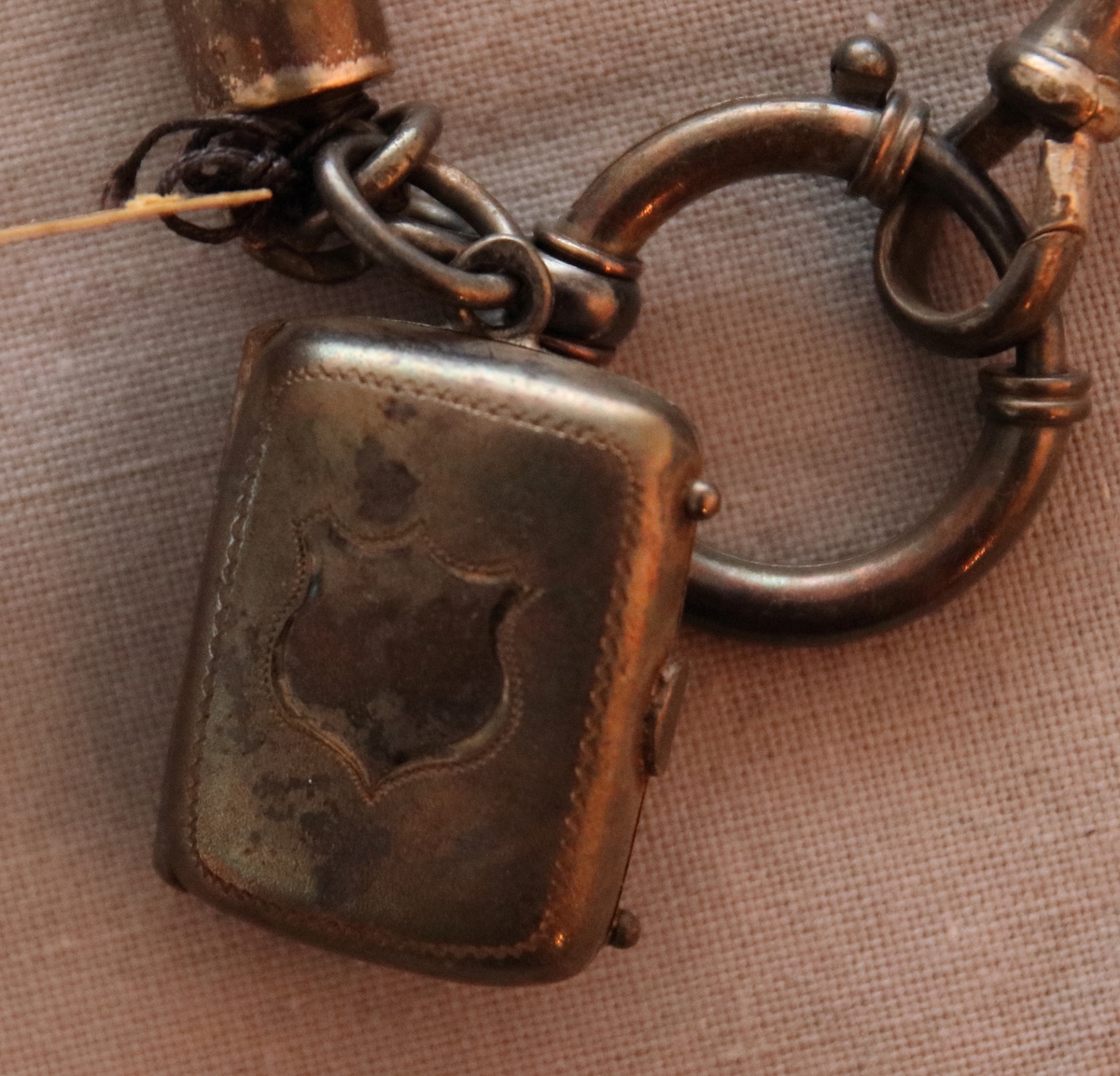 Urkedja av hår med silverbeslag. Med fyrkantig berlock med ingraverade blommor på ena sidan och en sköld på en den andra. Med en platta med ingraverat ”Minne”. - Stämpel B 7 = 1904, W. övriga stämplar oläsbara. -