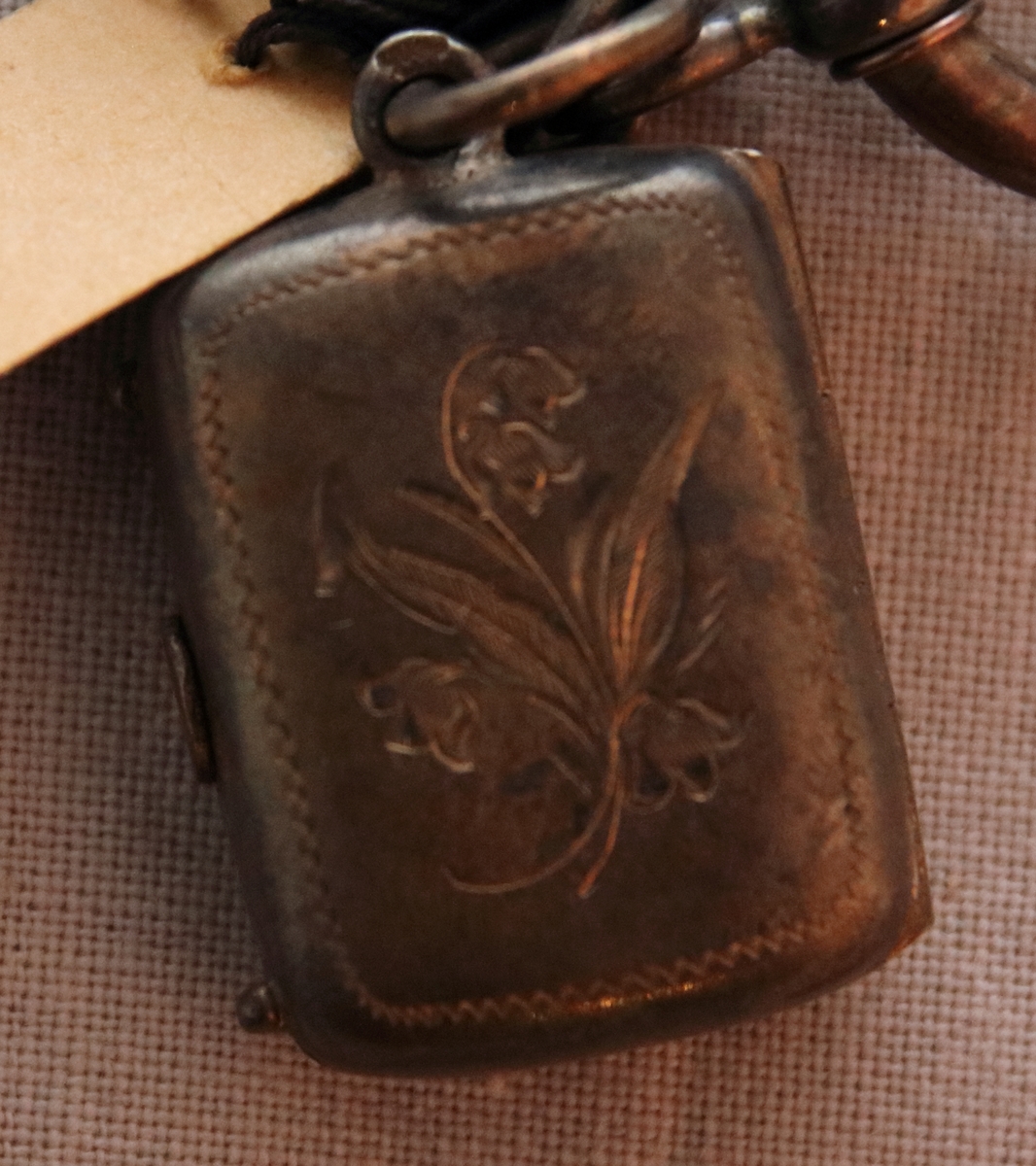 Urkedja av hår med silverbeslag. Med fyrkantig berlock med ingraverade blommor på ena sidan och en sköld på en den andra. Med en platta med ingraverat ”Minne”. - Stämpel B 7 = 1904, W. övriga stämplar oläsbara. -