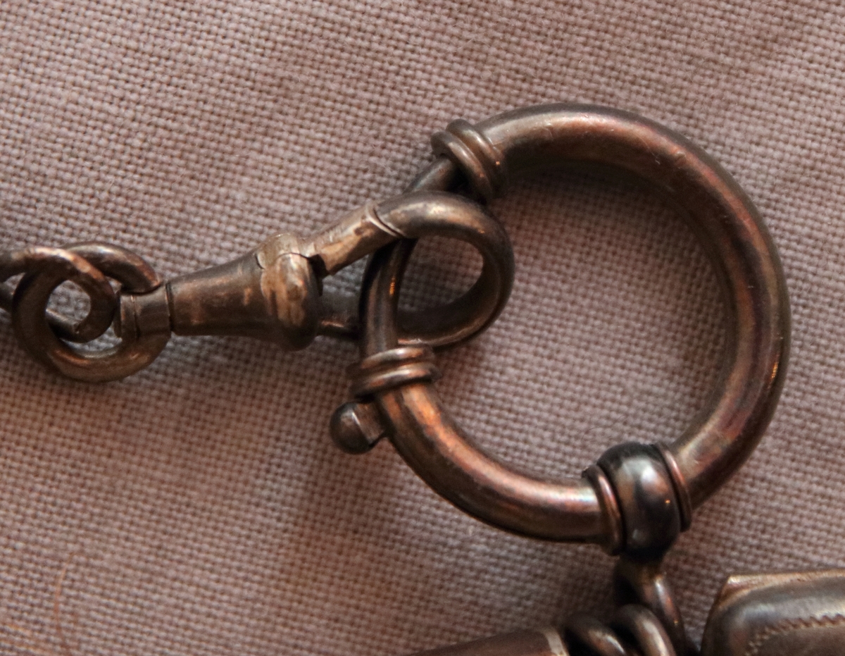 Urkedja av hår med silverbeslag. Med fyrkantig berlock med ingraverade blommor på ena sidan och en sköld på en den andra. Med en platta med ingraverat ”Minne”. - Stämpel B 7 = 1904, W. övriga stämplar oläsbara. -