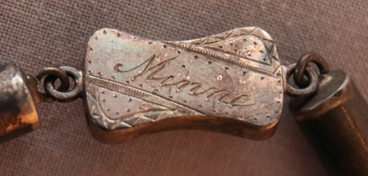 Urkedja av hår med silverbeslag. Med fyrkantig berlock med ingraverade blommor på ena sidan och en sköld på en den andra. Med en platta med ingraverat ”Minne”. - Stämpel B 7 = 1904, W. övriga stämplar oläsbara. -