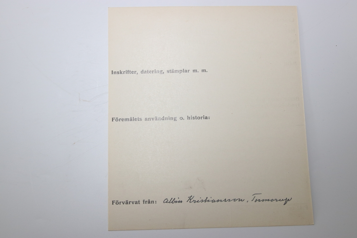 Oval dosa av silver. Med ett lock med gångjärn. Ytterkanten på ovansidan av locket har en cisilerad bård av stiliserade blad. I mitten av locket står initialerna "B. S. D. " och "G. A. S." . Asken är stämplad på insidan av botten med bokstäverna "MOB" (Michael Olof Barkman,1813-1851, Varberg) och med "N4" (år 1843) samt två svårtydda stämplar.