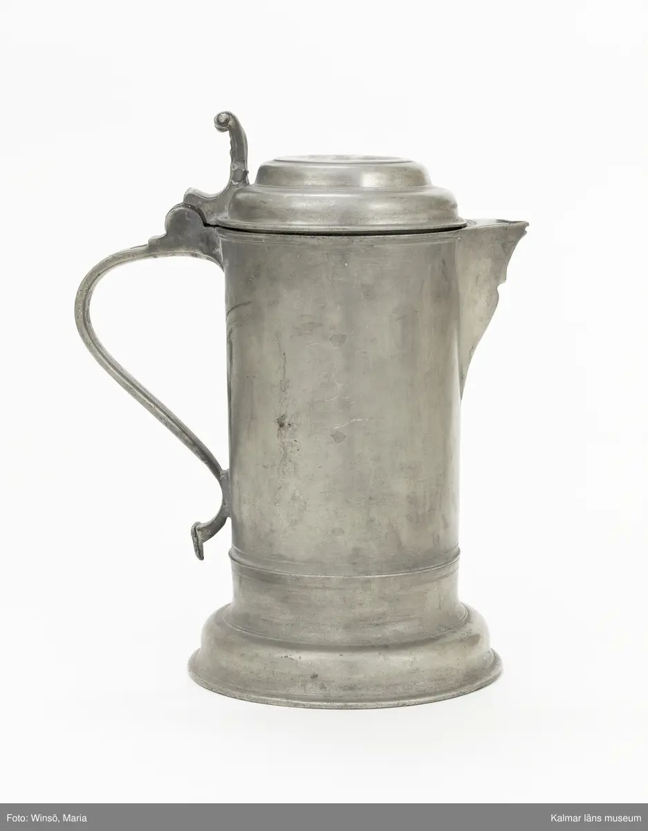 KLM 7267. Kanna, skänkkanna. Av tenn. Cylindrisk kanna med snås, lock och hänkel med tumgrepp. På locket inskription: Håkon Hakonson 1667. På grepen upptill 3 stämplar: Kalmar, två mästarstämplar, LS= Lars Sigfridsson. Använd för nattvardsvin men troligen från början för profant bruk.