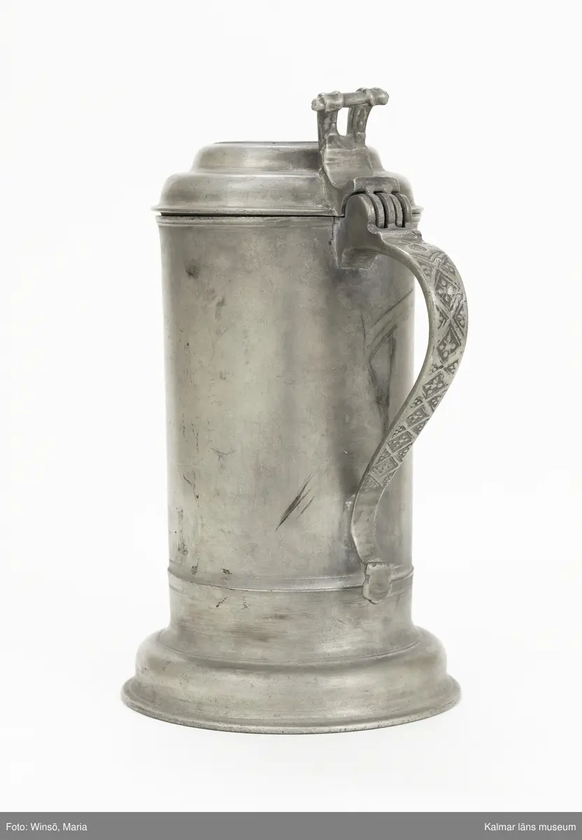 KLM 7267. Kanna, skänkkanna. Av tenn. Cylindrisk kanna med snås, lock och hänkel med tumgrepp. På locket inskription: Håkon Hakonson 1667. På grepen upptill 3 stämplar: Kalmar, två mästarstämplar, LS= Lars Sigfridsson. Använd för nattvardsvin men troligen från början för profant bruk.