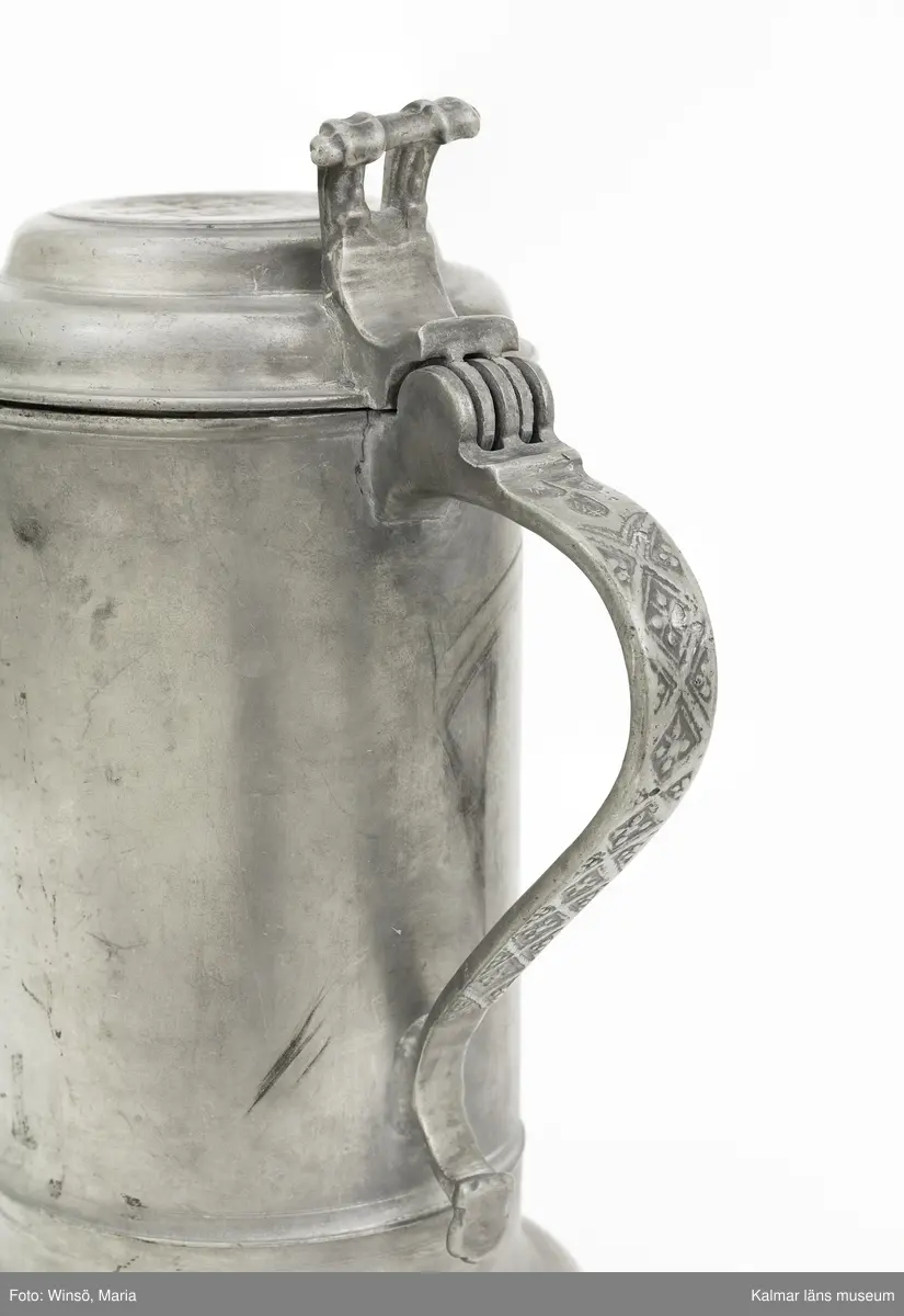 KLM 7267. Kanna, skänkkanna. Av tenn. Cylindrisk kanna med snås, lock och hänkel med tumgrepp. På locket inskription: Håkon Hakonson 1667. På grepen upptill 3 stämplar: Kalmar, två mästarstämplar, LS= Lars Sigfridsson. Använd för nattvardsvin men troligen från början för profant bruk.
