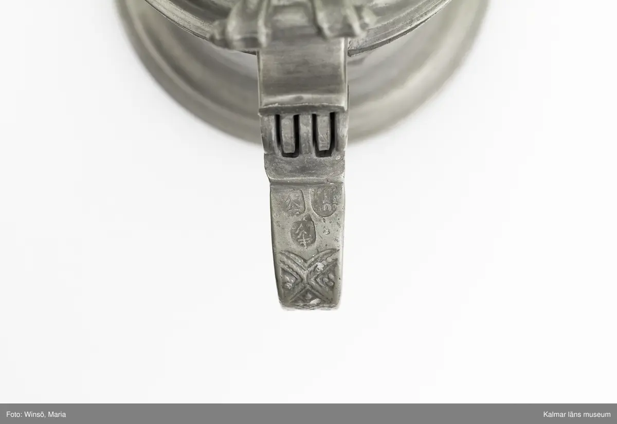 KLM 7267. Kanna, skänkkanna. Av tenn. Cylindrisk kanna med snås, lock och hänkel med tumgrepp. På locket inskription: Håkon Hakonson 1667. På grepen upptill 3 stämplar: Kalmar, två mästarstämplar, LS= Lars Sigfridsson. Använd för nattvardsvin men troligen från början för profant bruk.