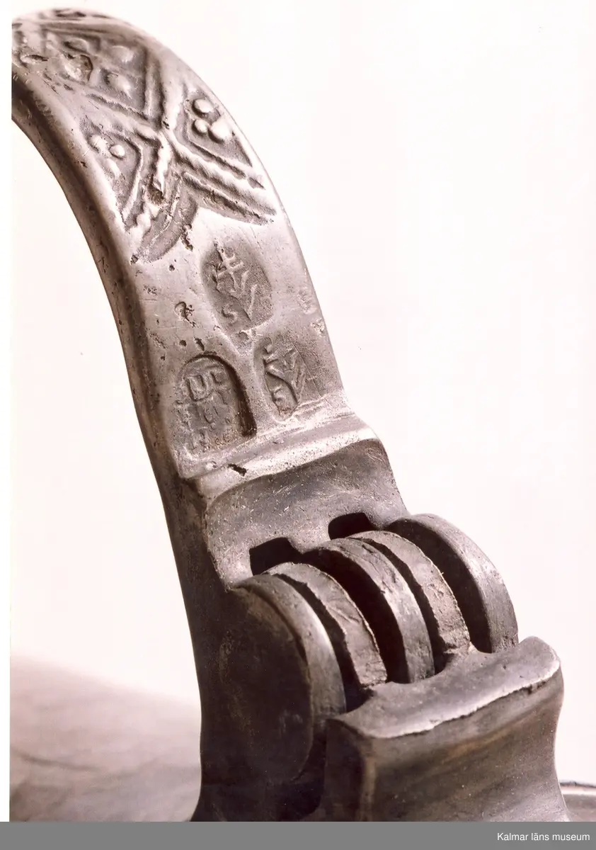 KLM 7267. Kanna, skänkkanna. Av tenn. Cylindrisk kanna med snås, lock och hänkel med tumgrepp. På locket inskription: Håkon Hakonson 1667. På grepen upptill 3 stämplar: Kalmar, två mästarstämplar, LS= Lars Sigfridsson. Använd för nattvardsvin men troligen från början för profant bruk.