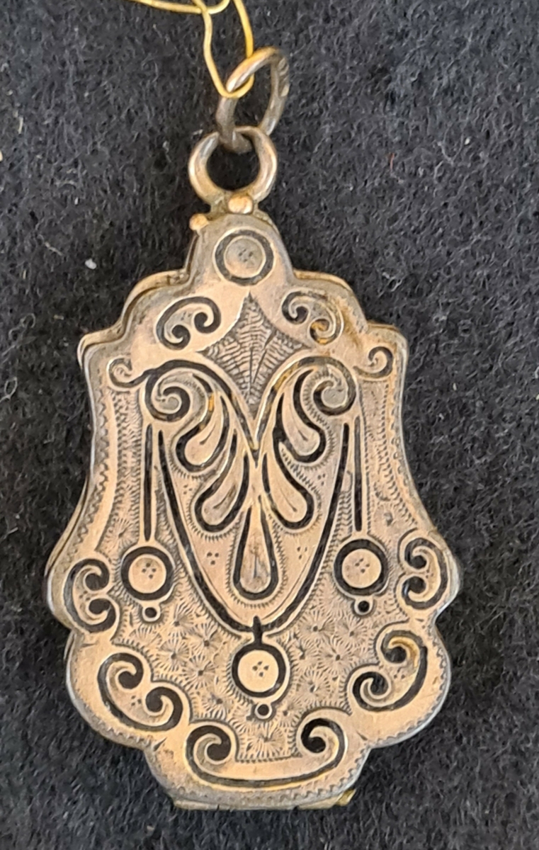 1. Avlång berlock (medaljong) med frimurarsymbol på baksidan. L. 2,9 cm. B. 2 cm.

2. Oval medaljong, troligtvis silver.Röd sten.  L. 2,7 cm  B. 2,4 cm