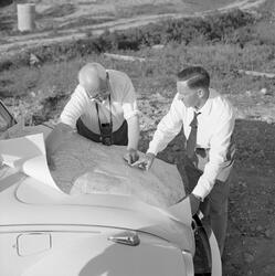 To menn studerer et kart de har liggende på panseret på en b