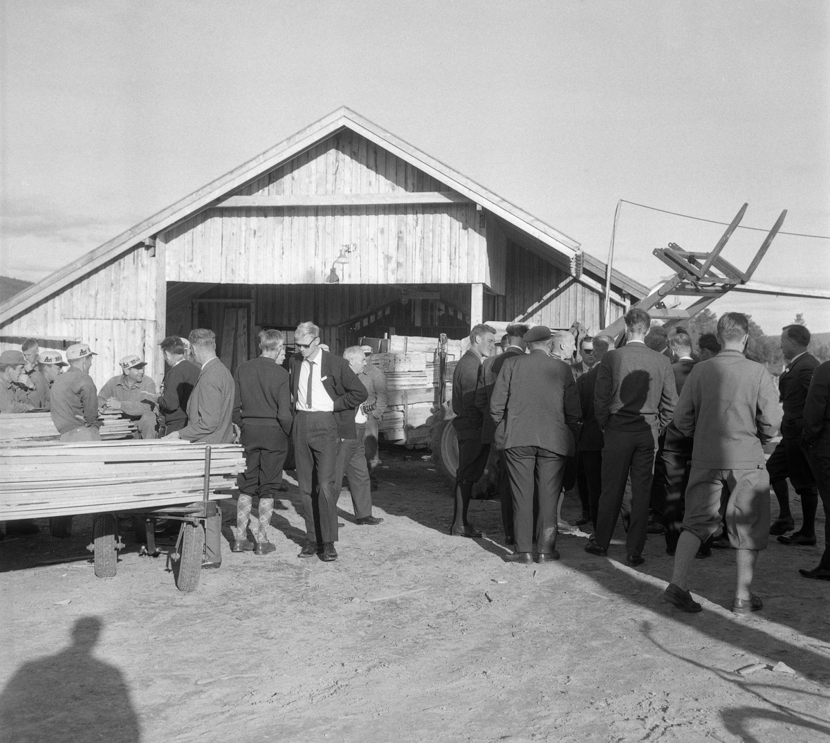 Fra en konferanse Direktoratet for statens skoger arrangerte i Trysil og Engerdal høsten 1964. Konferanseprogrammet hadde både en befaringsdel, der deltakerne fikk se hvordan statsskogene i området ble drevet, og en sekvens med foredrag og diskusjoner om mekaniseringa og de konsekvensene den kunne få for skogsarbeiderne. Dette fotografiet er tatt utenfor et av husene på Drevsjøsaga, som var en viktig del av virksomheten i Femund forvaltning. Her møttes arbeidskledde sagbruksarbeidere og dresskledde konferansedektakere.

Under fanen «Opplysninger» finnes regionavisa Østlendingens oppsummering av de faglige diskusjonene konferansedeltakerne hadde om mekanisering og sysselsetting.