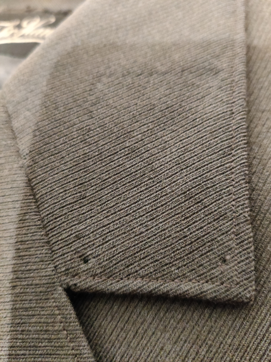 Grågrønn uniform med liggende krave og fire lommer, ridebukse og skilue (Finn Quales modell). Uniformen har bruksmerker, særlig på kraven. Luen er slitt, foret har løsnet. Alle gradstegn og knapper er fjernet fra jakken. God kvalitet på stoffet, muligens offisersuniform. (NB: Fremstår som grå på bildene, men har i virkeligheten en blass militærgrønn farge.)