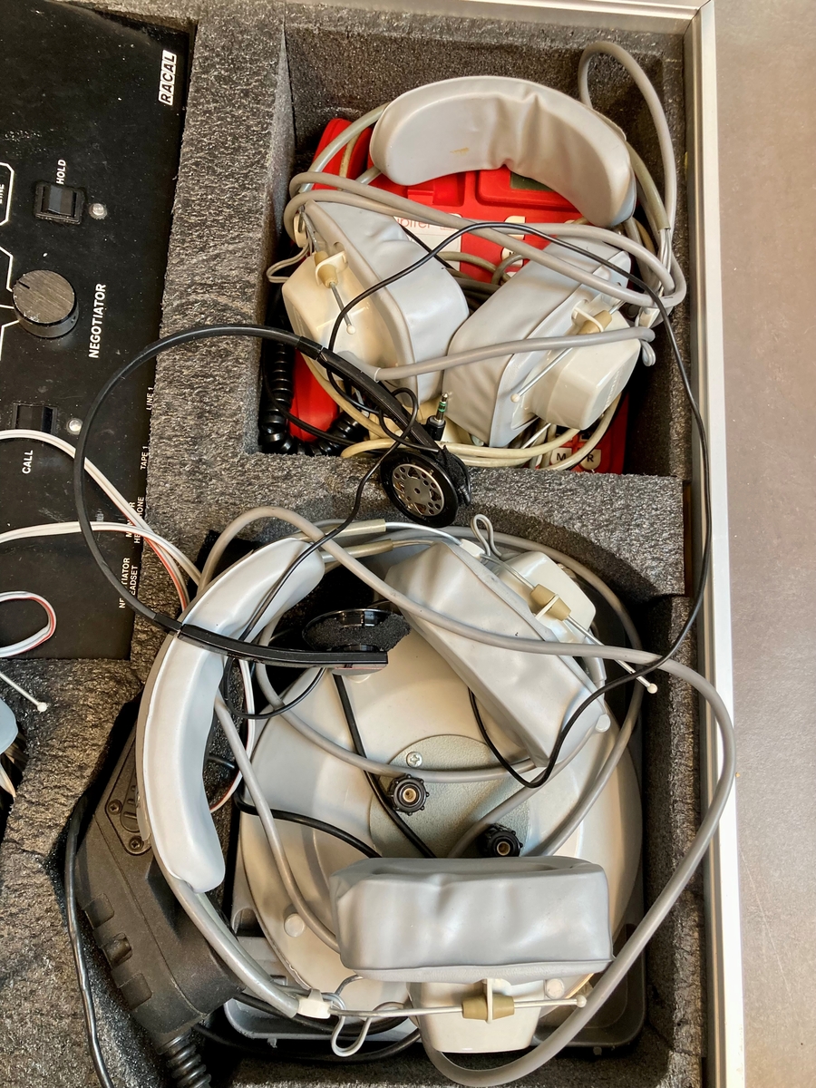 Koffert i metall som inneholder telefon og telefonsentral, opptaksutstyr og flere øretelefoner, lange telefonledninger, samt noe verktøy og kontorrekvisita, som skrujern, tapetkniv, tusjer, skrujern notatpapir, stifter, ekstra batterier mm.