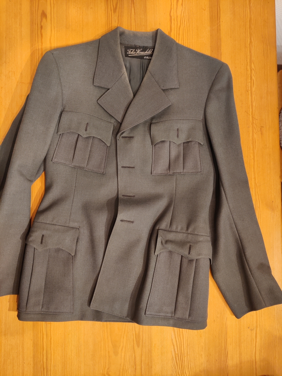 Grågrønn uniform med liggende krave og fire lommer, ridebukse og skilue (Finn Quales modell). Uniformen har bruksmerker, særlig på kraven. Luen er slitt, foret har løsnet. Alle gradstegn og knapper er fjernet fra jakken. God kvalitet på stoffet, muligens offisersuniform. (NB: Fremstår som grå på bildene, men har i virkeligheten en blass militærgrønn farge.)