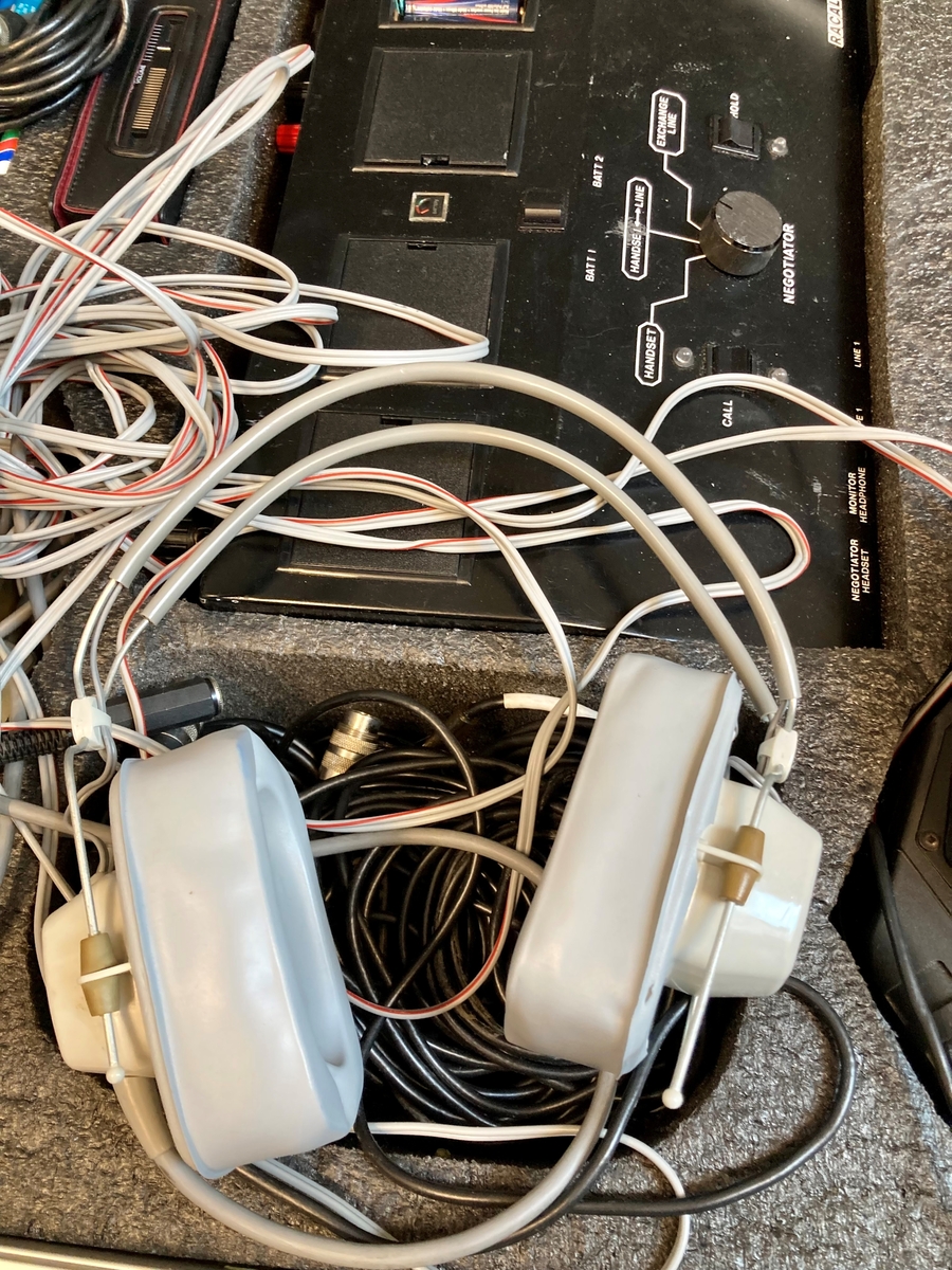 Koffert i metall som inneholder telefon og telefonsentral, opptaksutstyr og flere øretelefoner, lange telefonledninger, samt noe verktøy og kontorrekvisita, som skrujern, tapetkniv, tusjer, skrujern notatpapir, stifter, ekstra batterier mm.