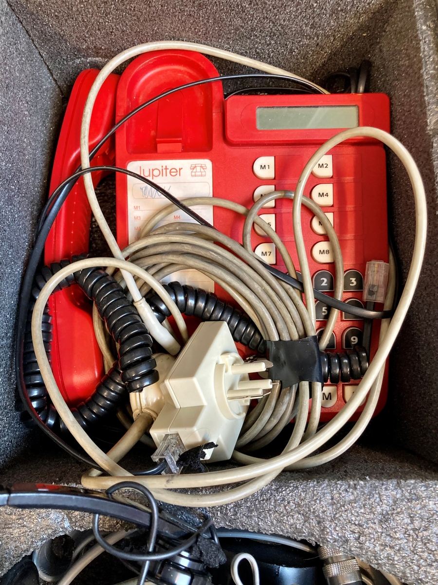 Koffert i metall som inneholder telefon og telefonsentral, opptaksutstyr og flere øretelefoner, lange telefonledninger, samt noe verktøy og kontorrekvisita, som skrujern, tapetkniv, tusjer, skrujern notatpapir, stifter, ekstra batterier mm.