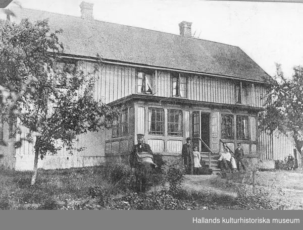 Brevkort avsänt 1906. Prästgården i Fagered en varm dag - både fönster och verandadörr är öppna. Kring verandatrappan är en familj samlad, sannolikt prästfamiljen. I förgrunden en uniformerad man bärande på en stor skinnväska, förmodligen en brevbärare.