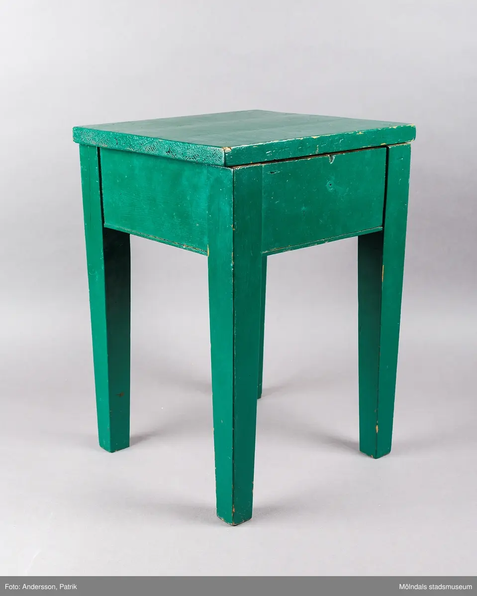 Grön sängpall/sängbord med förvaring. Pallen är 43 centimeter hög och 30 centmeter bred. Den är tillverkad i trä och målad i mörkgrönt. 

Gåva: Föreningen Gåreviks Barnkoloni. Pallen har stått i sovsalen. Varje barn hade en pall vid sin säng, som de kunde förvara sina privata tillhörigheter i.