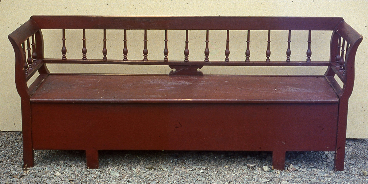 Rödmålad pinnsoffa med svarvade balusterformade pinnar i ryggen.
Något svängda sidostycken.