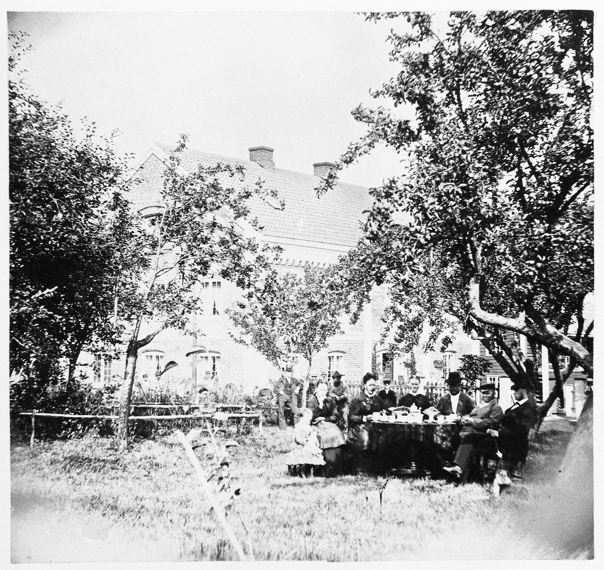 Gruppebilde fra Øvre (Søndre) Hammerstad i Totenvika ca. 1877. Bildet er tatt i hagen med hovedbygningen i bakgrunnen. Ved bordet fra venstre: Marie (Maien) Evensdtr. Gihle (1874-1936, g.m. Bernhard Rognerud, dernest hennes mor Helene Olsdtr Hammerstad (g.m. Even E. Gihle på Dyrin), Marie Pedersdtr. Hammerstad (1829-1899, g.m. Ole Jensen Hammerstad), Dorte Helene Jensdtr. Hammerstad (1828-1923, ugift), Fredrik Jensen Hammerstad (1832-1898, ugift), Ole Jensen Hammerstad (1824-1896, eier av gården), Even Evensen Gihle på Dyrin (1853-1919). I bakgrunnen ni personer, alle ukjente.