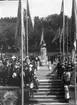 Fotografi i samband med invigningen av Brahe-bysten på Gränna torg 1916. Flaggor och en folksamling kantar vägen från Brahegatan upp mot bysten.