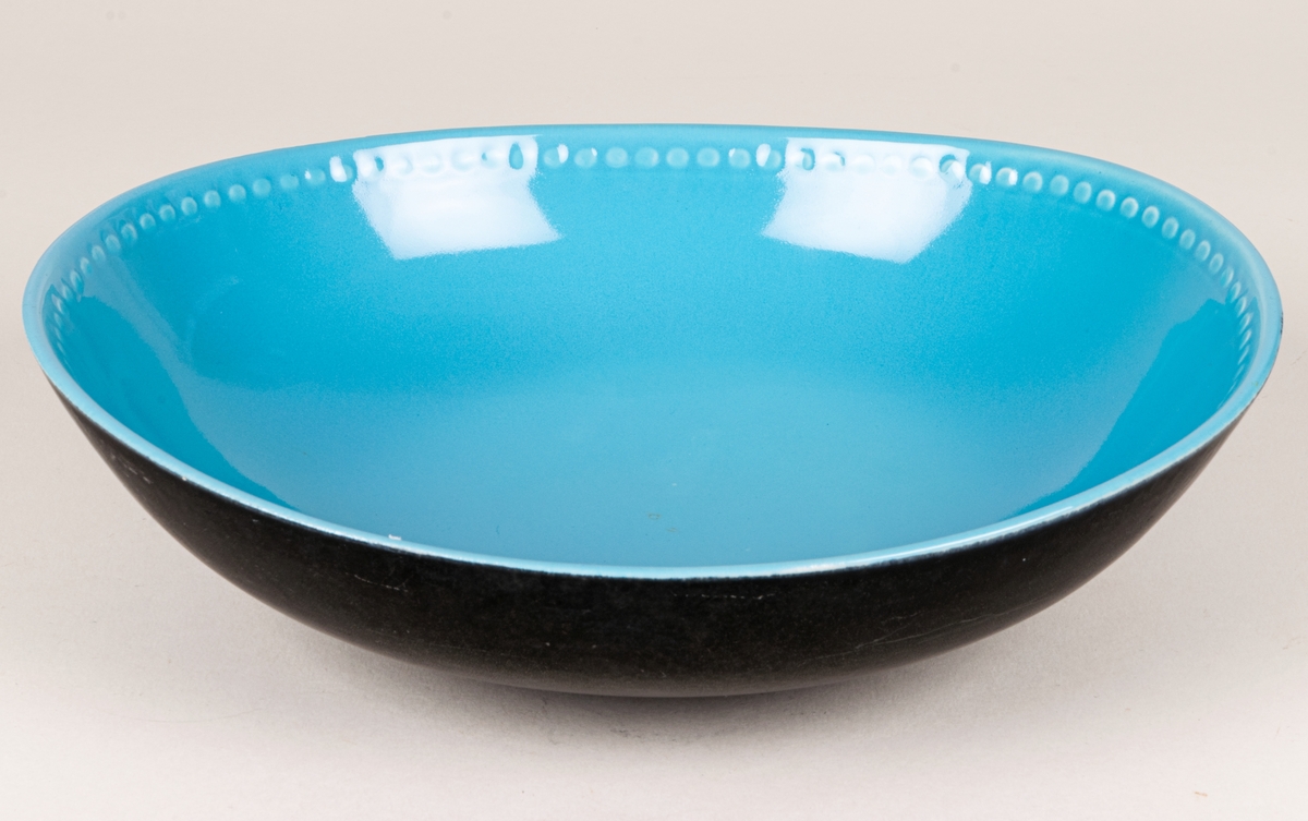Större oval skål i flintgods med dekor Indiana i modell LE2, forrmgiven av Arthur Percy för Gefle porslin 1957. Insidan har turkos glasyr, utsidan har den matta svarta glasyren Negro. Längs skålens kant på insidan finns upphöjda dekorativa prickar i godset.