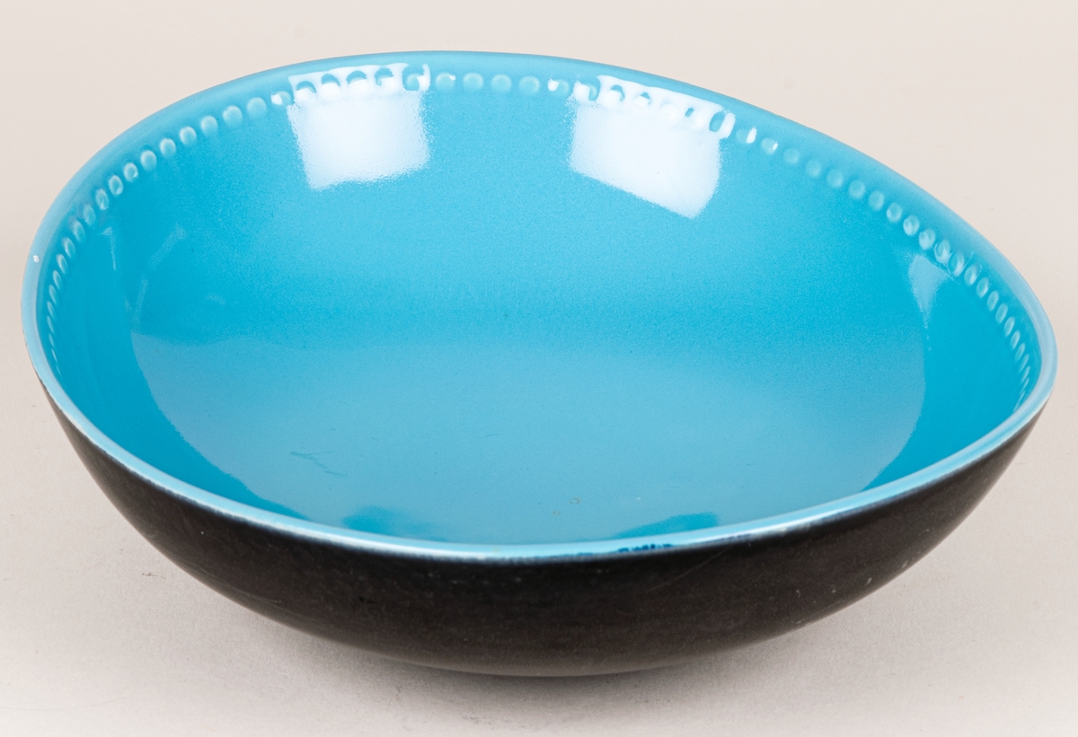 Större oval skål i flintgods med dekor Indiana i modell LE2, forrmgiven av Arthur Percy för Gefle porslin 1957. Insidan har turkos glasyr, utsidan har den matta svarta glasyren Negro. Längs skålens kant på insidan finns upphöjda dekorativa prickar i godset.