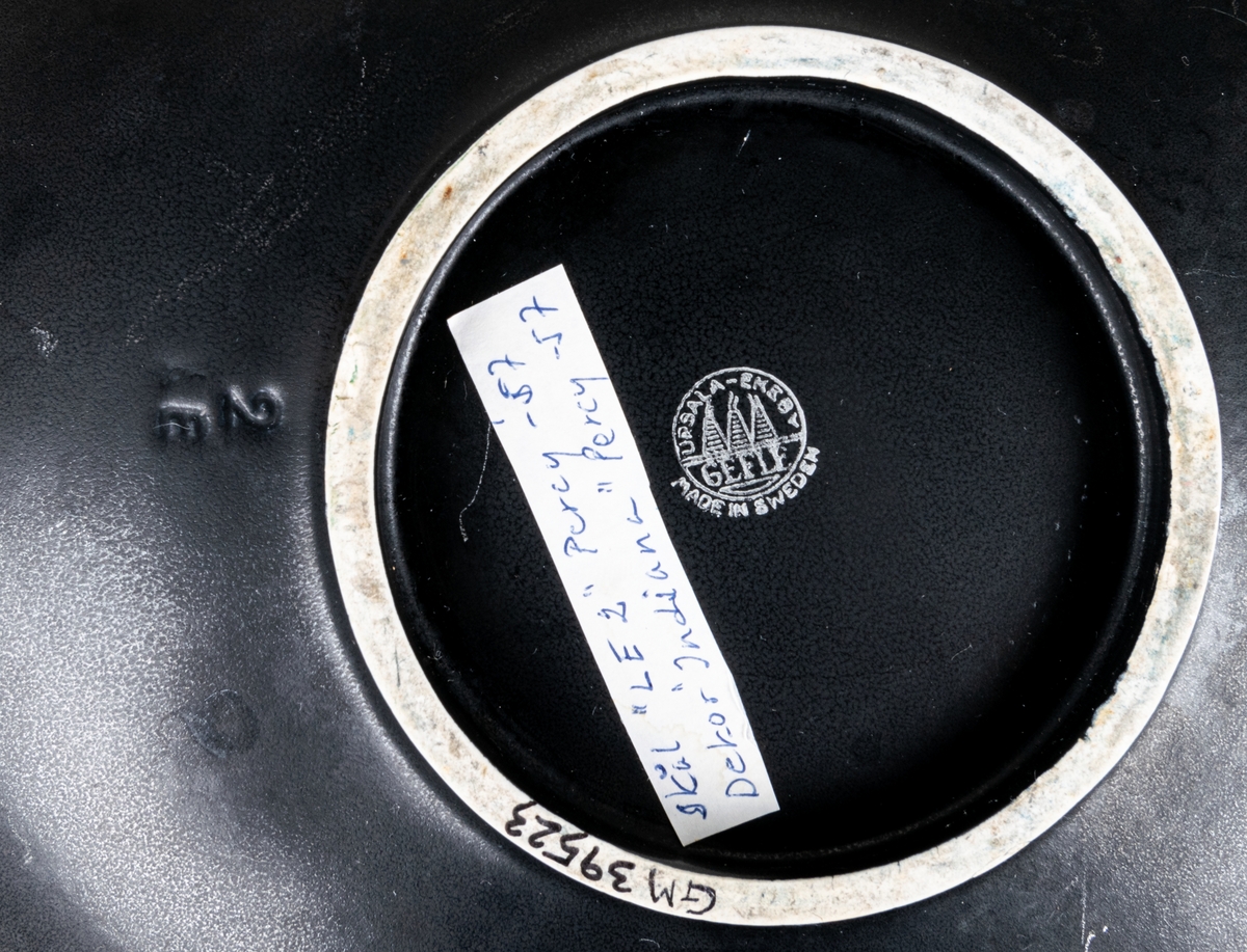 Större oval skål i flintgods med dekor Indiana i modell LE2, forrmgiven av Arthur Percy för Gefle porslin 1957. Insidan har turkos glasyr, utsidan har den matta svarta glasyren Negro. Längs skålens kant på insidan finns upphöjda dekorativa prickar i godset.