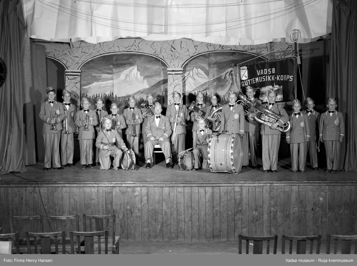 Vadsø guttemusikk-korps på scenen i Vårbrudd. Dirigent Olav L. Holmen sitter i midten foran musikantene. Bildet er tatt på 1950-tallet. Kilde: Fotosamlinga ved Troms og Finnmark fylkesbibliotek.
Musikanter 1 Albert Moe, 2 Ragnar Wara, 3 Per Norvik, 4 Fredrik Lebesby, 5 Rolf Berg, 6 Terje Waaktor, 7 Terje Joki, 8 Dirigent Olav Holmen, 9 Atle Eimjellen, Ivar Nelsvik, 11 Svein Holsbø, 12 Jarl Methi, 13 Andreas Berg, 14 Harald Sørum, 15 Tor Gundersen, 16 Erling Henriksen, 17 Kjell Gundersen, 18 Frits Pettersen, 19 Tor Rushfeldt.
