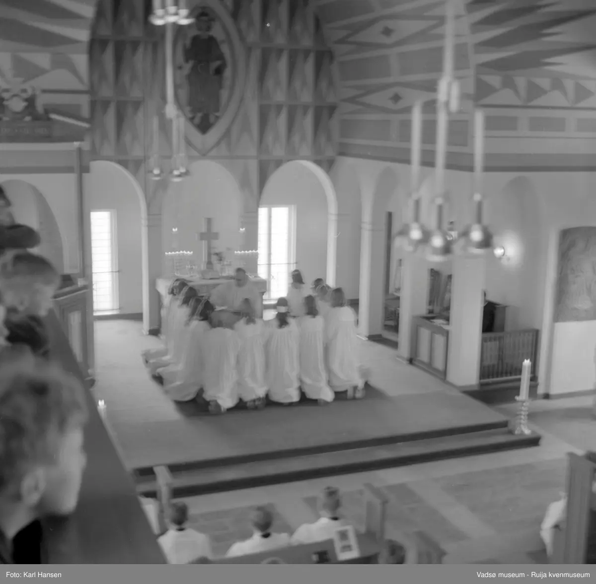 Vadsø kirke, interiør 10.5.1969. Alteret med knelende konfirmanter. Kirka er tegnet av arkitekt Magnus Poulssson, og ble innviet i 1958,