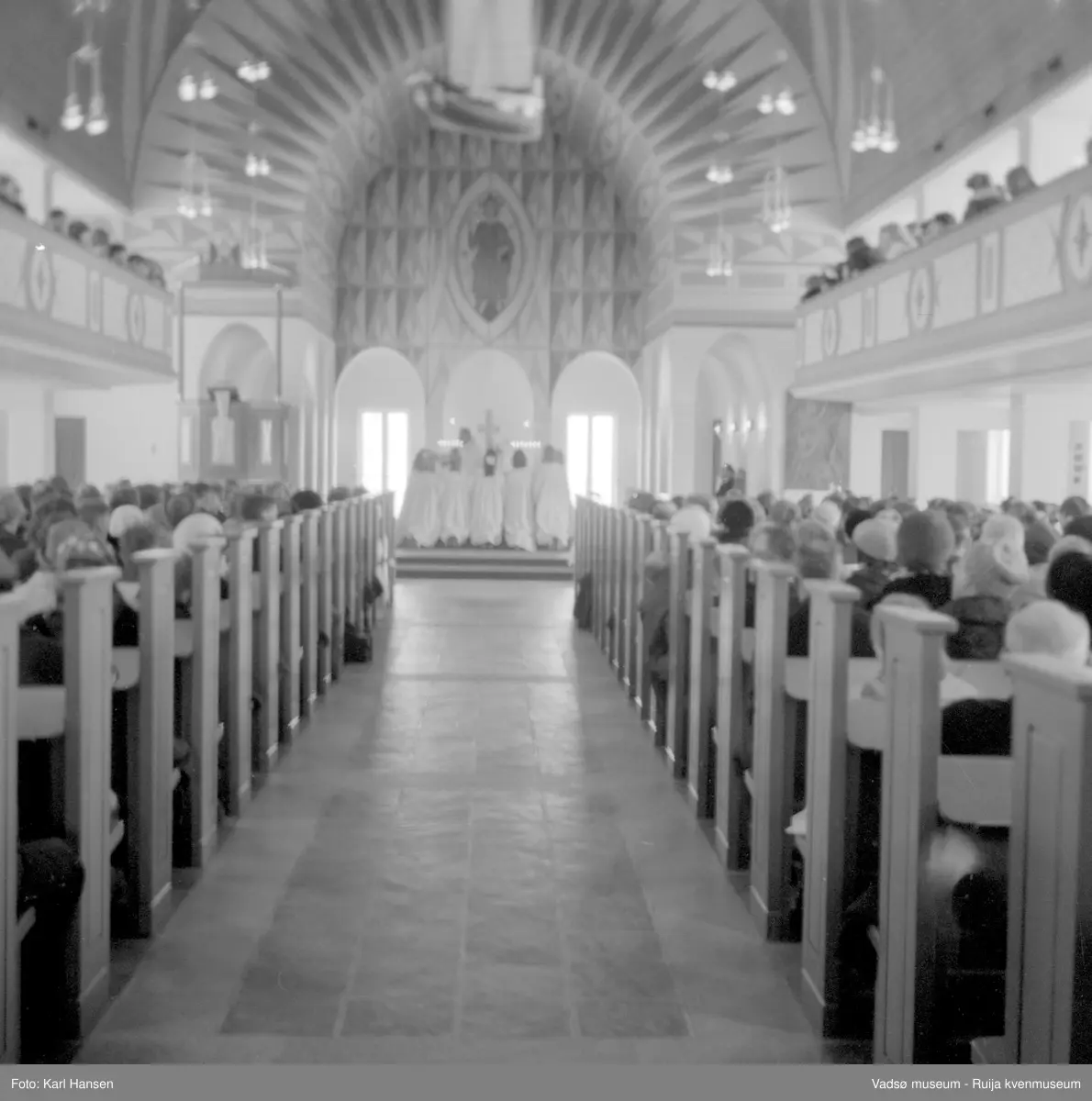 Vadsø kirke, interiør under konfirmasjon10.5.1969. Vadsø kirke er tegnet av arkitekt Magnus Poulsson og utsmykket av Greta Thiis. Kirka ble vigslet i 1958.