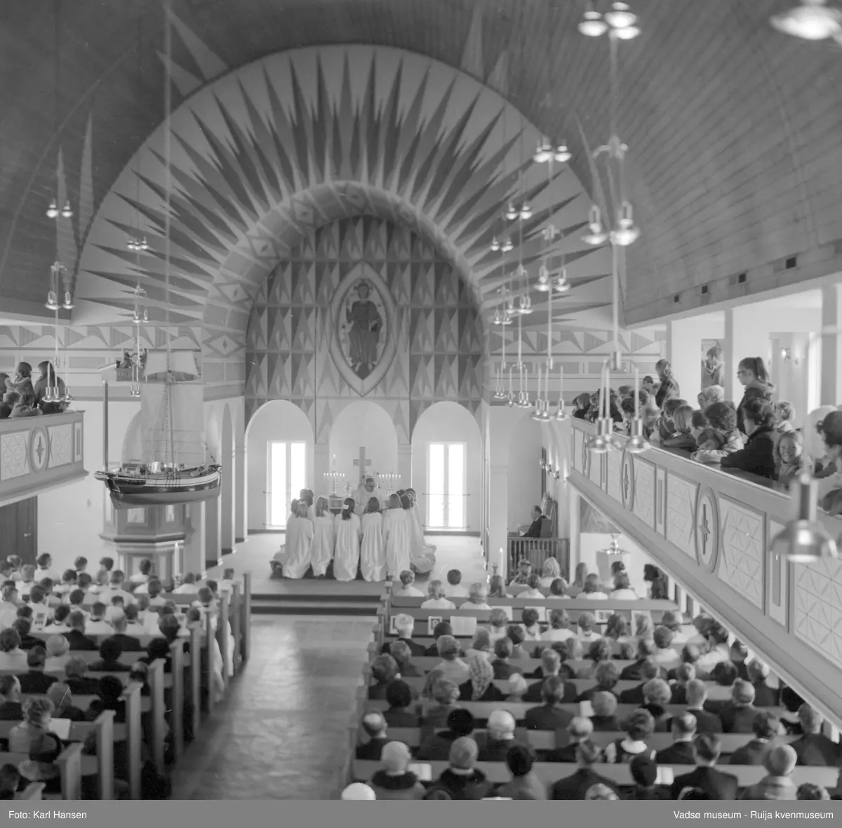 Vadsø kirke, interiør 10.5.1969. Konfirmanter kneler ved alteret. Kirka ble vigslet i 1958, utsmykket av Greta Thiis.