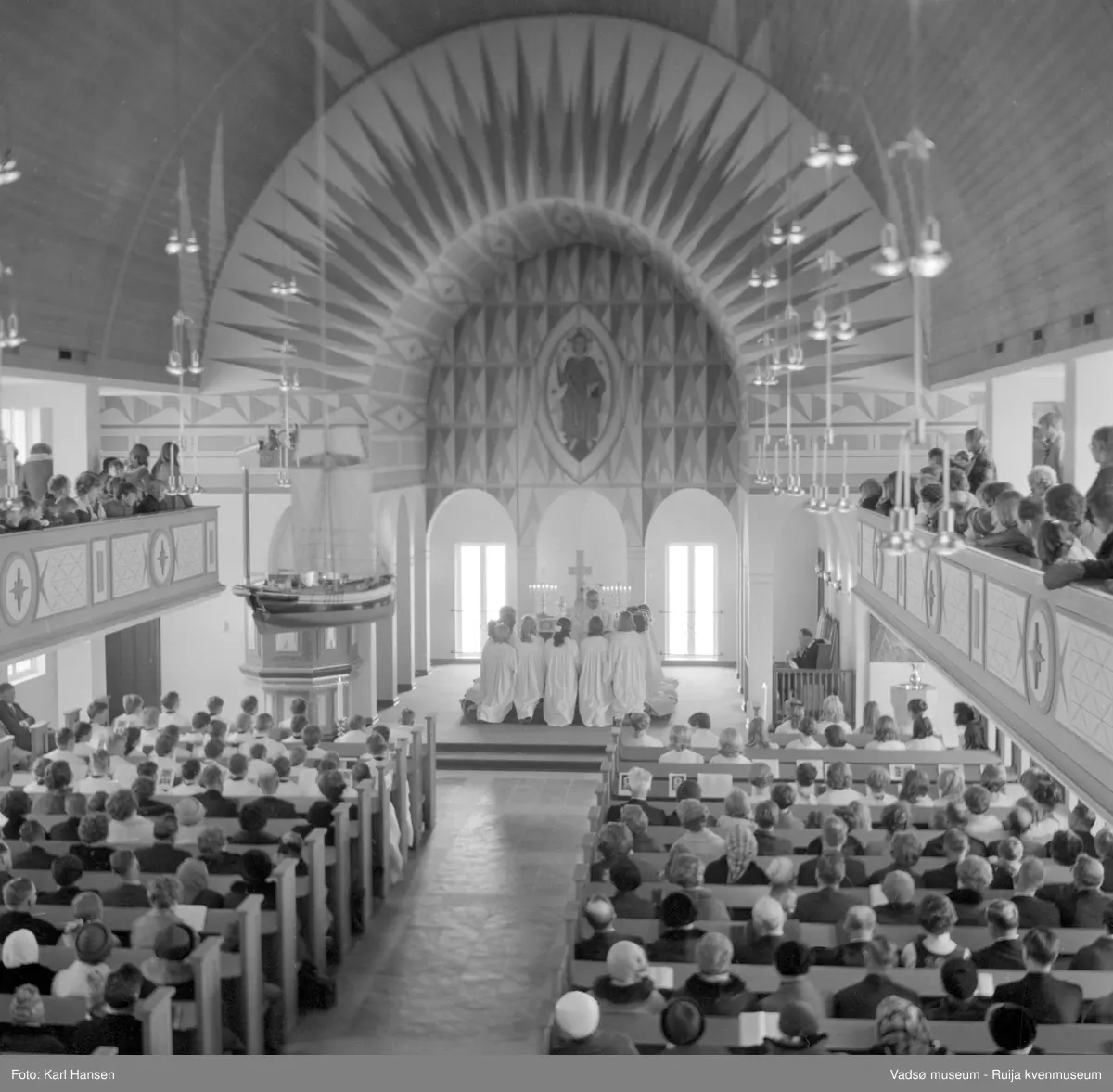 Vadsø  kirke interiør 1.5.1969. Konfirmasjon, konfirmanter kneler ved alteret. Kirka ble tegnet av arkitekt Magnus Poulsson og vigslet i 1958.