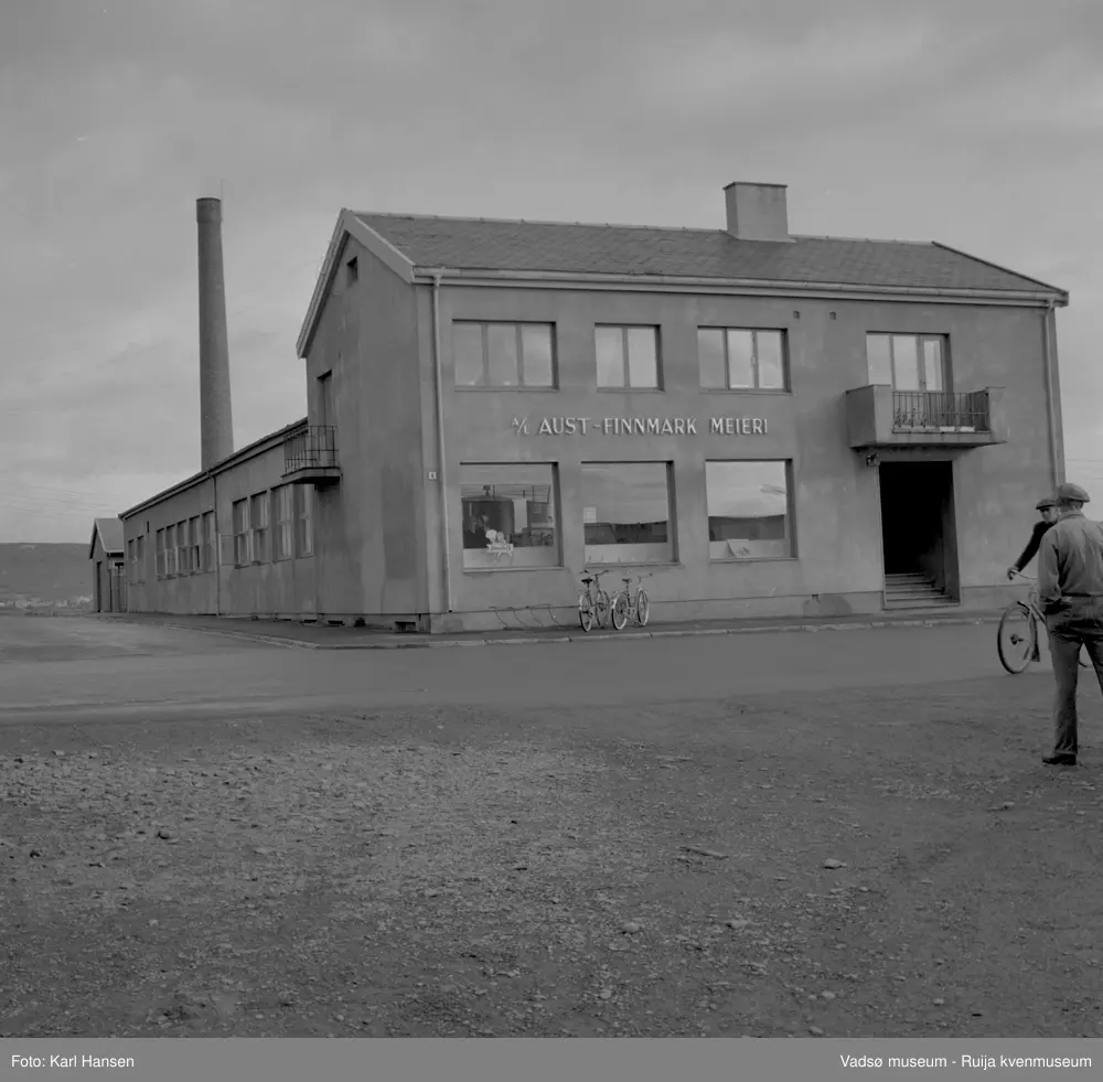 A/L Aust-Finnmark Meieri, 1962 i Vadsø. Bildet er tatt mot øst.  
Arbeidet med å få meieri til Vadsø ble påbegynt før krigen.  Ønsket var å få et meieri som kunne dekke Nord-Varanger-Tanadistriktet.  Andelslaget Aust-Finnmark Meieri ble stiftet 28.juni 1947 i Nyborg.  
Aust- Finnmark Meieri ble oppført i Tollbugata i 1949; arkitekt Monrad Heggen m hovedentreprenør Brdr. Aronsen.
Oppstart skulle finne sted ca 1. oktober 1949, og i mai ble det ansatt en meieriarbeider; Richard Korbi fra Vadsø.
Kilde: "A.L Aust-Finnmark Meieri 25 års jubileum 1949-1974; styreformann Ivar Johnsen, Tana mai 1974"