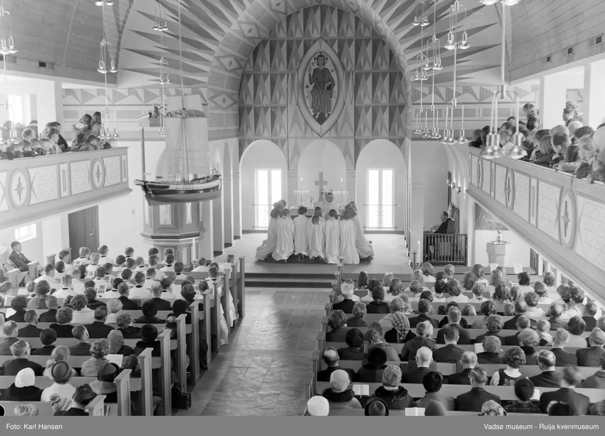 Vadsø kirke, interiør 10.5.1969. Konfirmasjon, konfirmanter kneler ved alteret. Kirka er tegnet av arkitekt Magnus Poulsson, vigslet i 1958.