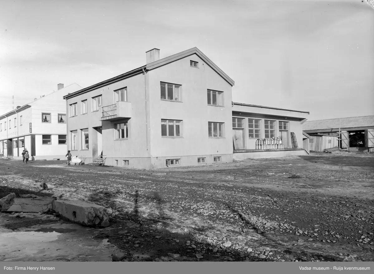 A/L Aust Finnmark Meieri. Bildet er tatt mot nordøst  og viser inngangspartiet, sydveggen  og lasterampen med stabler av melkespann. Til venstre i bildet H.F. Esbensens forretningsbygg med Apoteket på hjørnet av Tollbugata/W.Andersensgate. Det er vårløsning i Tollbugata. 
Aust- Finnmark Meieri ble oppført i 1949; arkitekt Monrad Heggen m hovedentreprenør Brdr. Aronsen