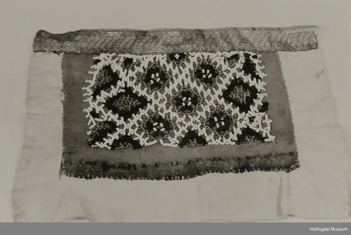 Håndsydd brystduk i lin, ull og silke med fløyelsband og glassperler i blomstermønster. Ubleika linlerret på baksida.
