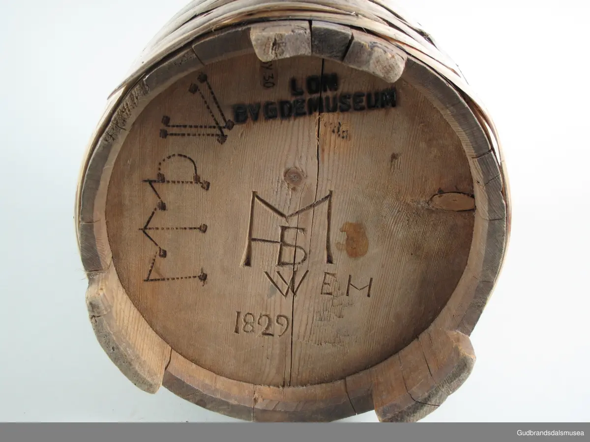 "Ølkrusforma kanne, stor, med kurve lok, som paa undersida har geomegtriske ornament og inskripsjon. Trulig brukt som smørform. Fraa privatsamling..." (Jvf. Katalog...1925).
Stavkanne brukt til servering av smør. Ca. 4,4 liter. 7 gjorder. Hank og hengslet lokk med lokkgrep. Lokket er festet med en tapp gjennom hank og lokkåpneren sine to ører. Lokket dreier seg ved hjelp av tretappen som fungerer som en aksel. Korpus hviler på tre staver, som er lengre enn de øvrige.
Dekor. Lokk med karveskurd og inskripsjoner på innsiden og svidekor på utsiden. Svidekor på korpus og hank. Liten kongle som lokkgrep.