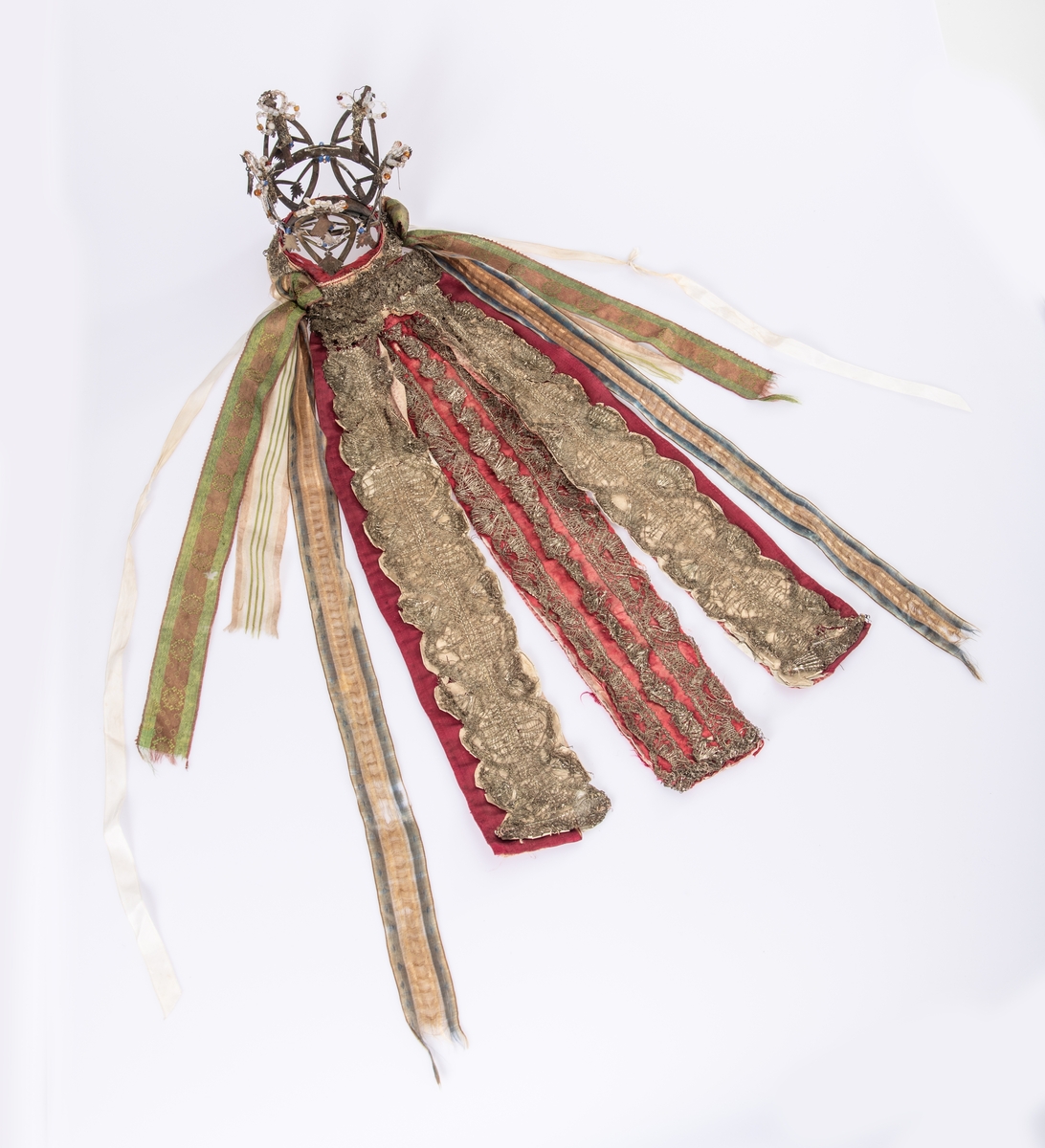 Brudekrone i metall med fem spir. Krona er pyntet med metallheng og glassperler. Det er påsydd valk nederst, med brodert bånd og metallknipling rundt valken.

Bak på det broderte båndet rundt valken, er det festet bånd. På midten er det et bredt bånd i rødt med metallkniplinger, med brede bånd med lys bunn og med en rød kant vendt ut fra den røde midtbåndet. Metallkniplinger er festet til de tre brede båndene. Deretter fire smalere bånd på hver side av de brede båndene. Disse er festet samlet med en liten sløyfe på det bredeste der det er festet på valken. 

En plastkam er påsydd valken sammen med to hvite, nyere bånd. Antagelig gjort i nyere tid for å feste krona og knyte under haka.