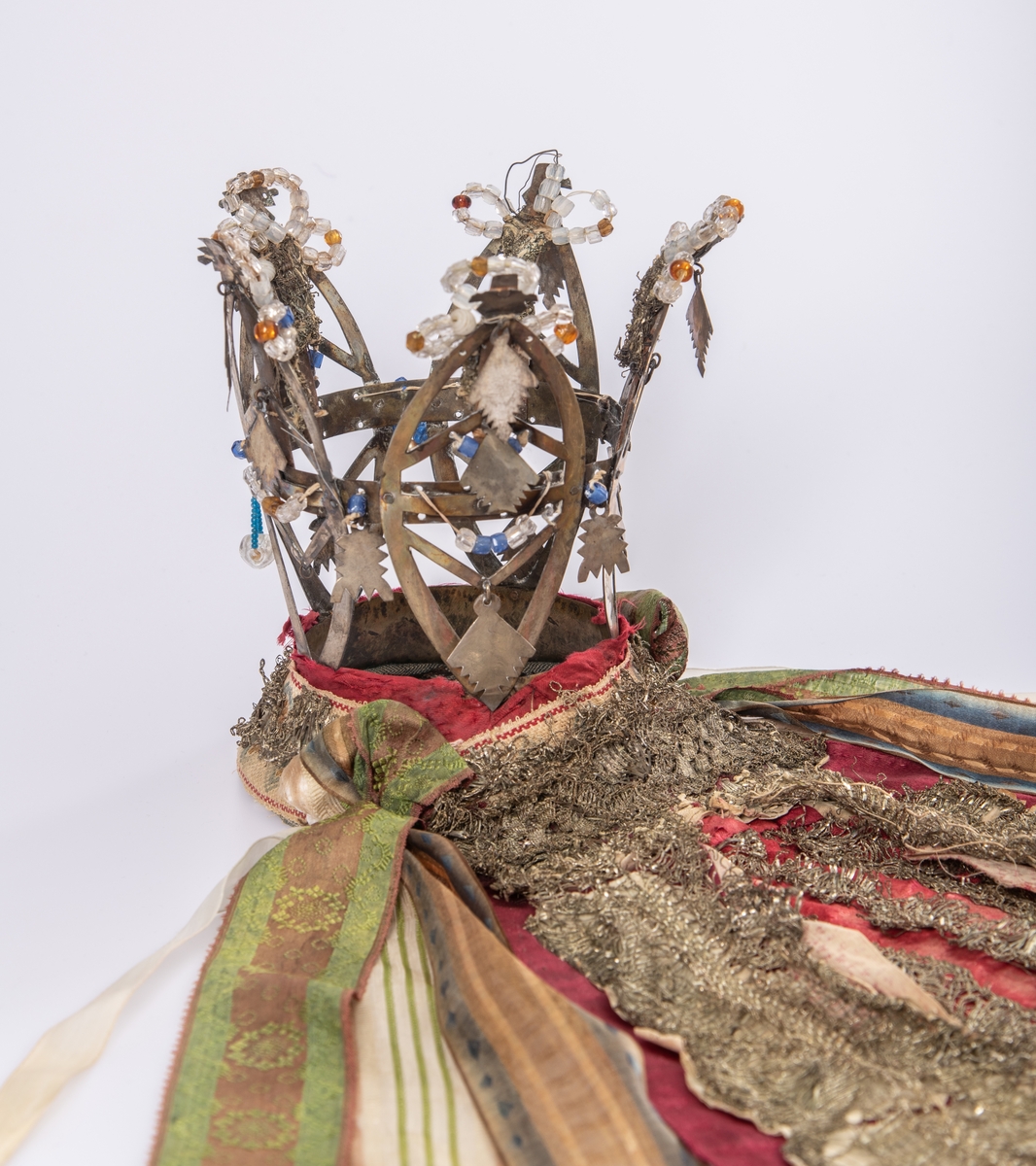 Brudekrone i metall med fem spir. Krona er pyntet med metallheng og glassperler. Det er påsydd valk nederst, med brodert bånd og metallknipling rundt valken.

Bak på det broderte båndet rundt valken, er det festet bånd. På midten er det et bredt bånd i rødt med metallkniplinger, med brede bånd med lys bunn og med en rød kant vendt ut fra den røde midtbåndet. Metallkniplinger er festet til de tre brede båndene. Deretter fire smalere bånd på hver side av de brede båndene. Disse er festet samlet med en liten sløyfe på det bredeste der det er festet på valken. 

En plastkam er påsydd valken sammen med to hvite, nyere bånd. Antagelig gjort i nyere tid for å feste krona og knyte under haka.