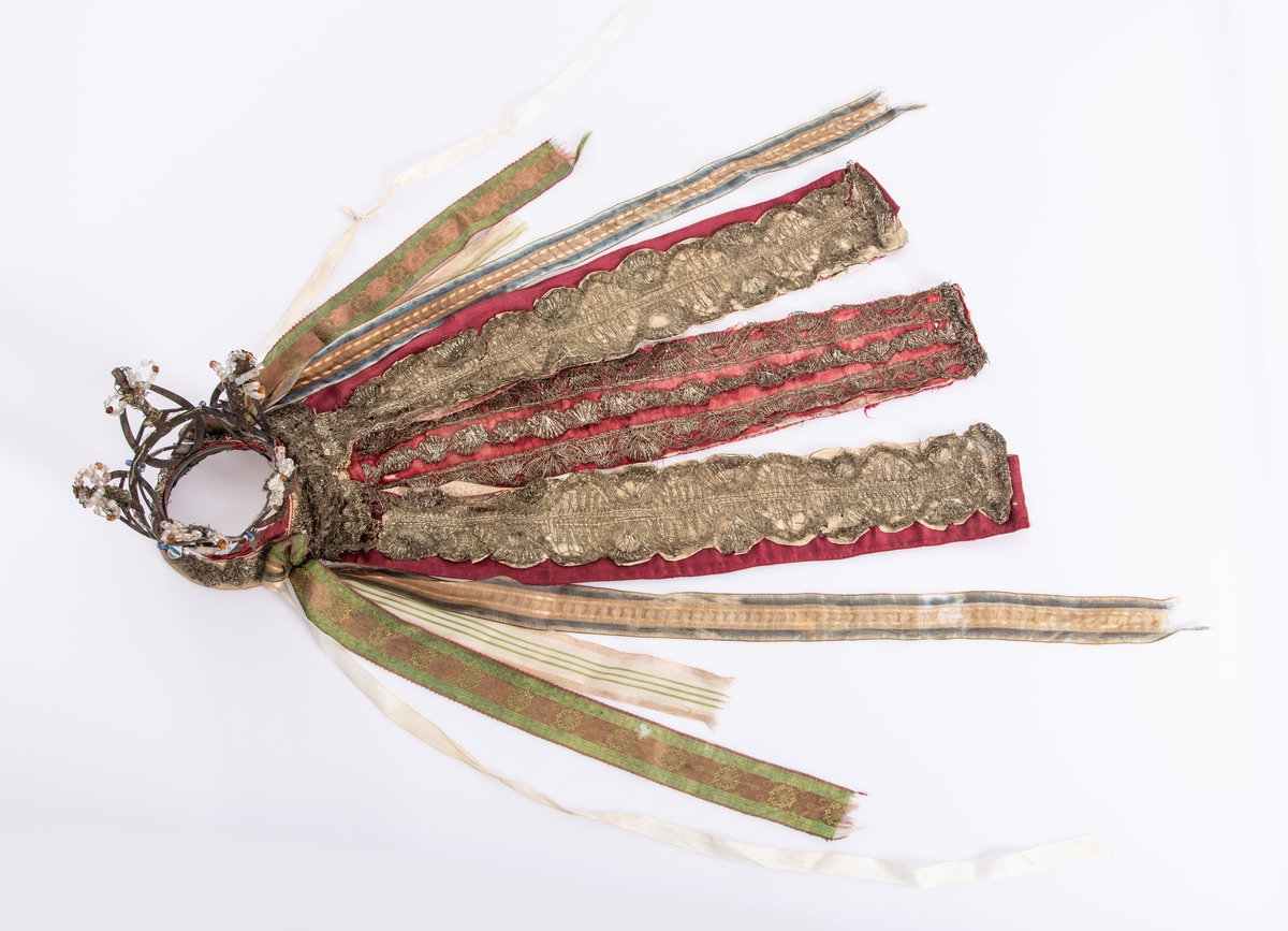 Brudekrone i metall med fem spir. Krona er pyntet med metallheng og glassperler. Det er påsydd valk nederst, med brodert bånd og metallknipling rundt valken.

Bak på det broderte båndet rundt valken, er det festet bånd. På midten er det et bredt bånd i rødt med metallkniplinger, med brede bånd med lys bunn og med en rød kant vendt ut fra den røde midtbåndet. Metallkniplinger er festet til de tre brede båndene. Deretter fire smalere bånd på hver side av de brede båndene. Disse er festet samlet med en liten sløyfe på det bredeste der det er festet på valken. 

En plastkam er påsydd valken sammen med to hvite, nyere bånd. Antagelig gjort i nyere tid for å feste krona og knyte under haka.