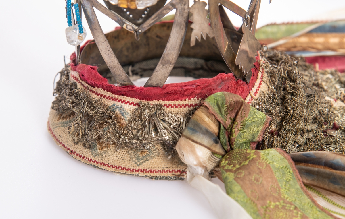 Brudekrone i metall med fem spir. Krona er pyntet med metallheng og glassperler. Det er påsydd valk nederst, med brodert bånd og metallknipling rundt valken.

Bak på det broderte båndet rundt valken, er det festet bånd. På midten er det et bredt bånd i rødt med metallkniplinger, med brede bånd med lys bunn og med en rød kant vendt ut fra den røde midtbåndet. Metallkniplinger er festet til de tre brede båndene. Deretter fire smalere bånd på hver side av de brede båndene. Disse er festet samlet med en liten sløyfe på det bredeste der det er festet på valken. 

En plastkam er påsydd valken sammen med to hvite, nyere bånd. Antagelig gjort i nyere tid for å feste krona og knyte under haka.