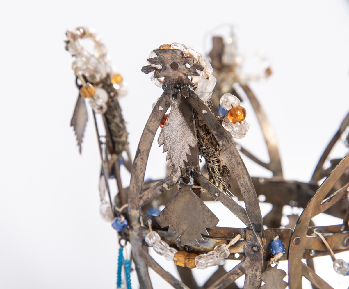 Brudekrone i metall med fem spir. Krona er pyntet med metallheng og glassperler. Det er påsydd valk nederst, med brodert bånd og metallknipling rundt valken.

Bak på det broderte båndet rundt valken, er det festet bånd. På midten er det et bredt bånd i rødt med metallkniplinger, med brede bånd med lys bunn og med en rød kant vendt ut fra den røde midtbåndet. Metallkniplinger er festet til de tre brede båndene. Deretter fire smalere bånd på hver side av de brede båndene. Disse er festet samlet med en liten sløyfe på det bredeste der det er festet på valken. 

En plastkam er påsydd valken sammen med to hvite, nyere bånd. Antagelig gjort i nyere tid for å feste krona og knyte under haka.