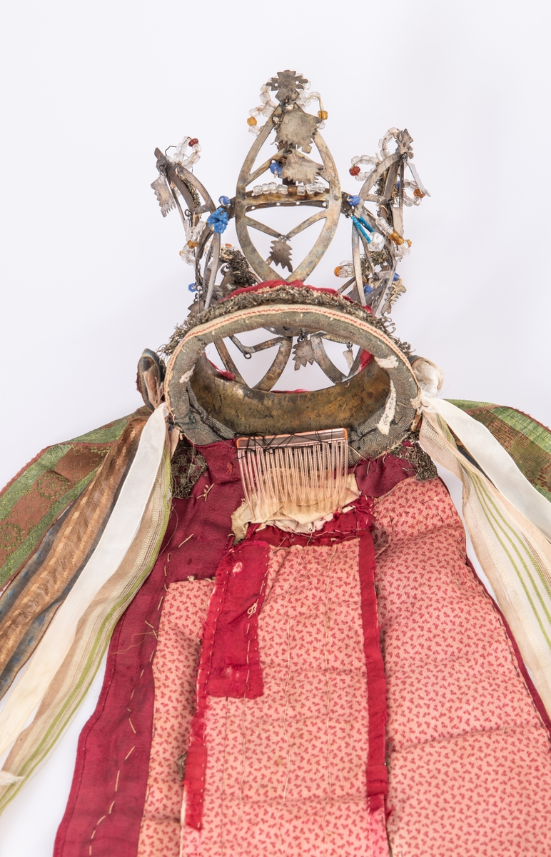 Brudekrone i metall med fem spir. Krona er pyntet med metallheng og glassperler. Det er påsydd valk nederst, med brodert bånd og metallknipling rundt valken.

Bak på det broderte båndet rundt valken, er det festet bånd. På midten er det et bredt bånd i rødt med metallkniplinger, med brede bånd med lys bunn og med en rød kant vendt ut fra den røde midtbåndet. Metallkniplinger er festet til de tre brede båndene. Deretter fire smalere bånd på hver side av de brede båndene. Disse er festet samlet med en liten sløyfe på det bredeste der det er festet på valken. 

En plastkam er påsydd valken sammen med to hvite, nyere bånd. Antagelig gjort i nyere tid for å feste krona og knyte under haka.